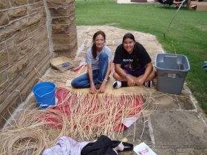 two people sitting on the ground with basket weaving materials